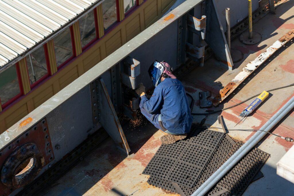 Male worker from behind on a construction site, welding the wall of a ship being restored