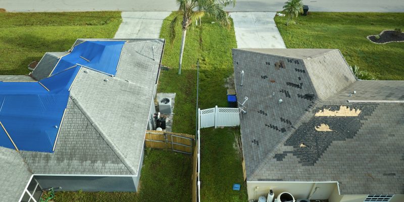 Aerial view of damaged in hurricane Ian house roof covered with blue protective tarp