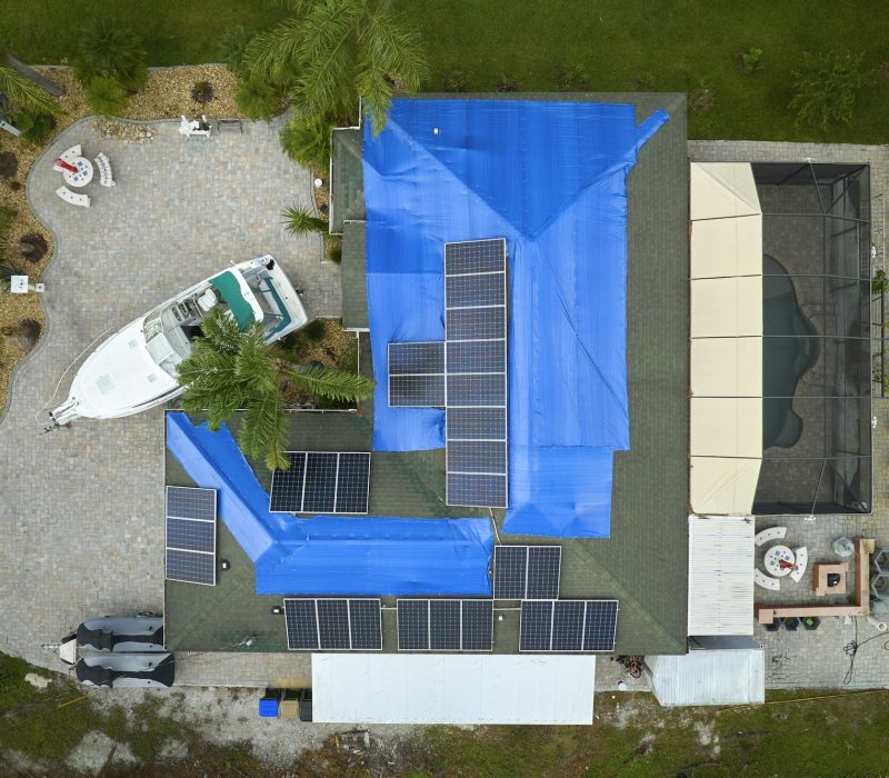 Aerial view of damaged in hurricane Ian house roof covered with blue protective tarp