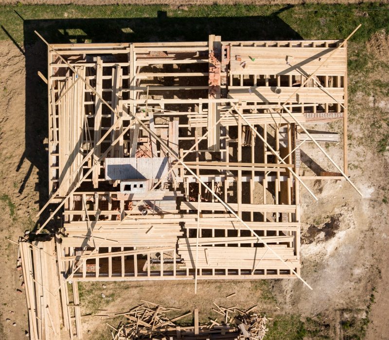 Aerial view of unfinished brick house with wooden roof frame structure under construction.